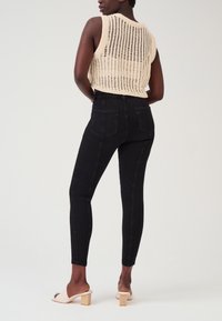 Zwarte skinny jeans met een hoge taille, voorzien van twee achterzakken en de zijnaad. Gecombineerd met een gebreide crèmekleurige mouwloze top.