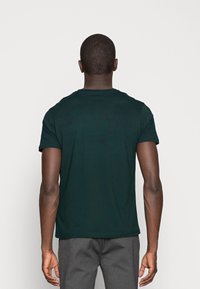 Mørkegrøn kortærmet t-shirt med rund halsudskæring, glat tekstur og et enkelt design, vist på en model set bagfra.