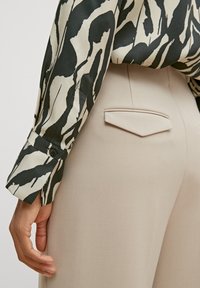 Long-sleeved shirt with a black and cream abstract pattern, paired with beige tailored pants featuring a small, angular back pocket detail.