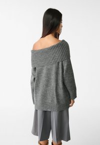 Grijze gebreide off-shoulder trui met geribbelde halslijn en manchetten, met een zachte textuur en een ontspannen pasvorm. Gecombineerd met grijze shorts.