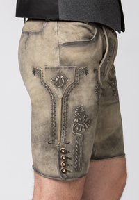 Pantaloni corti in pelle con una finitura tessurizzata e usurata. Presentano cuciture ornate, motivi decorativi e bottoni metallici di lato.