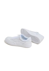 Białe trampki wykonane z gładkiej skóry, z teksturowanymi detalami, płaskimi sznurowadłami i wzorzystą gumową podeszwą. Logo umieszczone po boku.