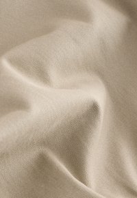 Tissu en coton beige avec une surface lisse, légèrement texturée, présentant des plis doux et un motif de tissage régulier.