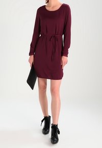 Bordeaux långärmad klänning med knyt i midjan, tillsammans med svarta ankelboots. Slät tygtextur, enkel design, knälång.