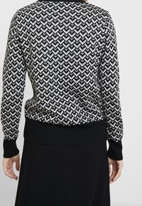 Maglione a righe in bianco e nero con un design a zigzag. Presenta maniche lunghe, un orlo a coste nera a vestibilità attillata e un collo rotondo.