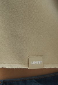 Étiquette beige Levi's cousue à l'ourlet d'un vêtement en maille beige au-dessus d'un jean en denim bleu.
