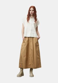 Camicia bianca a maniche corte con bottoni abbinata a una lunga gonna utilitaria color sabbia con tasche laterali e stivali alla caviglia beige.