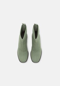 Botas de tobillo de punto verde con una textura suave, punta redondeada y laterales elásticos. Con tirador en la parte trasera para facilitar el uso. Suela plana negra.