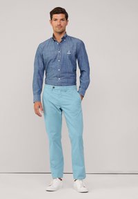 Chinos de algodón azul claro combinados con una camisa de mezclilla oscura de botones que presenta un logotipo bordado y zapatillas blancas.