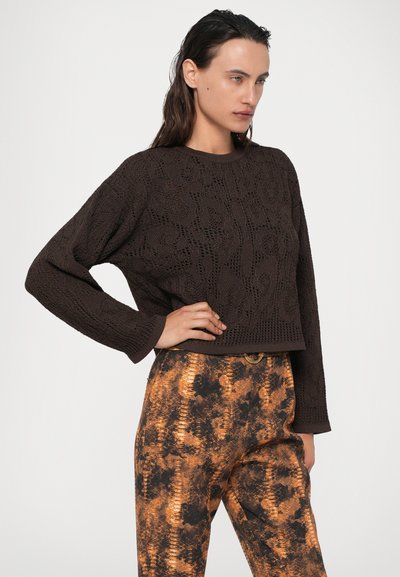 Maglione marrone lavorato a maglia con un motivo testurizzato, dotato di maniche lunghe e design corto, abbinato a pantaloni arancioni a fantasia a vita alta.