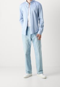 Hellblaues Hemd mit Knöpfen und Kragen, das das "BOSS"-Logo trägt; kombiniert mit hellen Jeans aus Denim und weißen Sneakern für einen lässigen Look.