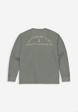 Olijfgroene overhemd met lange mouwen, geribbelde manchetten en een ronde hals, met daarop de witte tekst "BUTCHER OF BLUE QUALITY CLOTHING CO" op de achterkant.