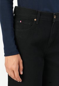Svarte denimjeans med en noe løs passform. Har en gullknapp, frontlommer og en liten trikolor-logo på lommen. Glatt tekstur.