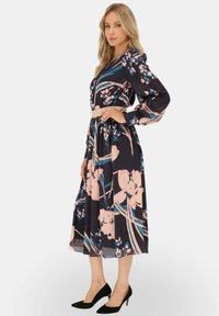 Granatowa sukienka w kwiaty z różowymi i niebieskimi wzorami, długimi bufkami, wcięciem w talii oraz spódnicą o średniej długości. Połączona z czarnymi szpilkami.