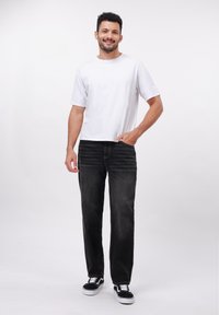 Camiseta blanca de manga corta y vaqueros negros de pierna recta, combinados con zapatillas blancas y negras. Diseño simple con un ajuste cómodo.