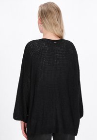 Maglione nero a maglia larga con una vestibilità ampia e maniche a pipistrello. Tessuto testurizzato e branding discreto sul collo posteriore.