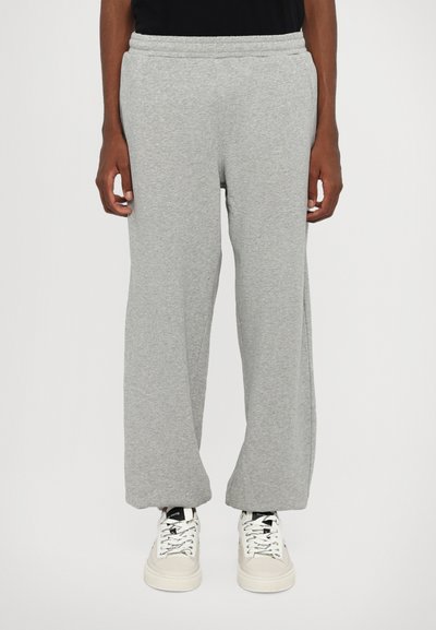 Grey sweatpants with a relaxed fit, made of soft, textured fabric. Features an elastic waistband and subtle stitching details. Worn with white sneakers.