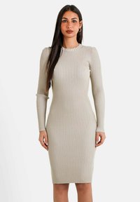 Ribbet beige kjole med lange ærmer, tætsiddende design, rund halsudskæring og knælang kant. Subtíl tekstur med en glat finish.