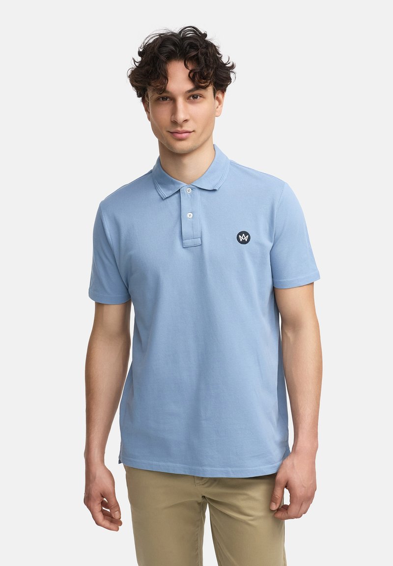 Lyseblå polo skjorte laget av bomull. Har krage, tre-knapplers knipling, og en liten svart logo på venstre bryst. Korte ermer.