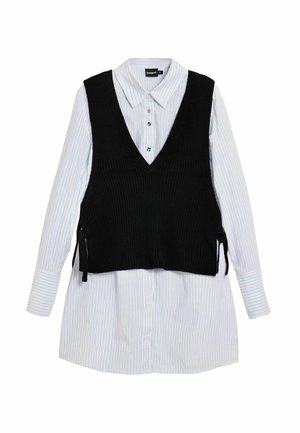 Abito camicia bianco a maniche lunghe con sottili strisce nere, sovrapposto a un gilet senza maniche nero lavorato a maglia con laccetti laterali.