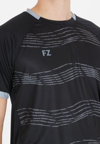 Musta urheilupaita, jossa on harmaita aaltoilevia viivoja ja vaaleanharmaat kaulus sekä hihansuut, rinnassa "FZ"-logo.