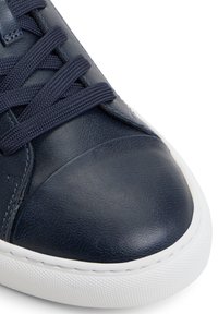 Sneaker in pelle blu marino con punta arrotondata, suola in gomma bianca e superficie texture. Presenta dettagli in tinta con lacci e sottili accenti di cucitura.