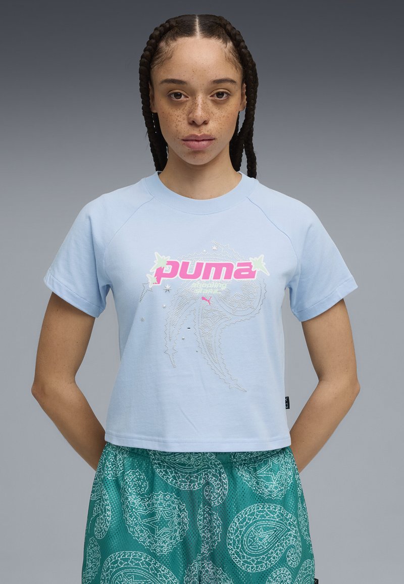 Camiseta corta de color azul claro con un logo "PUMA" en rosa y acentos gráficos decorativos; mangas cortas con un ajuste relajado.