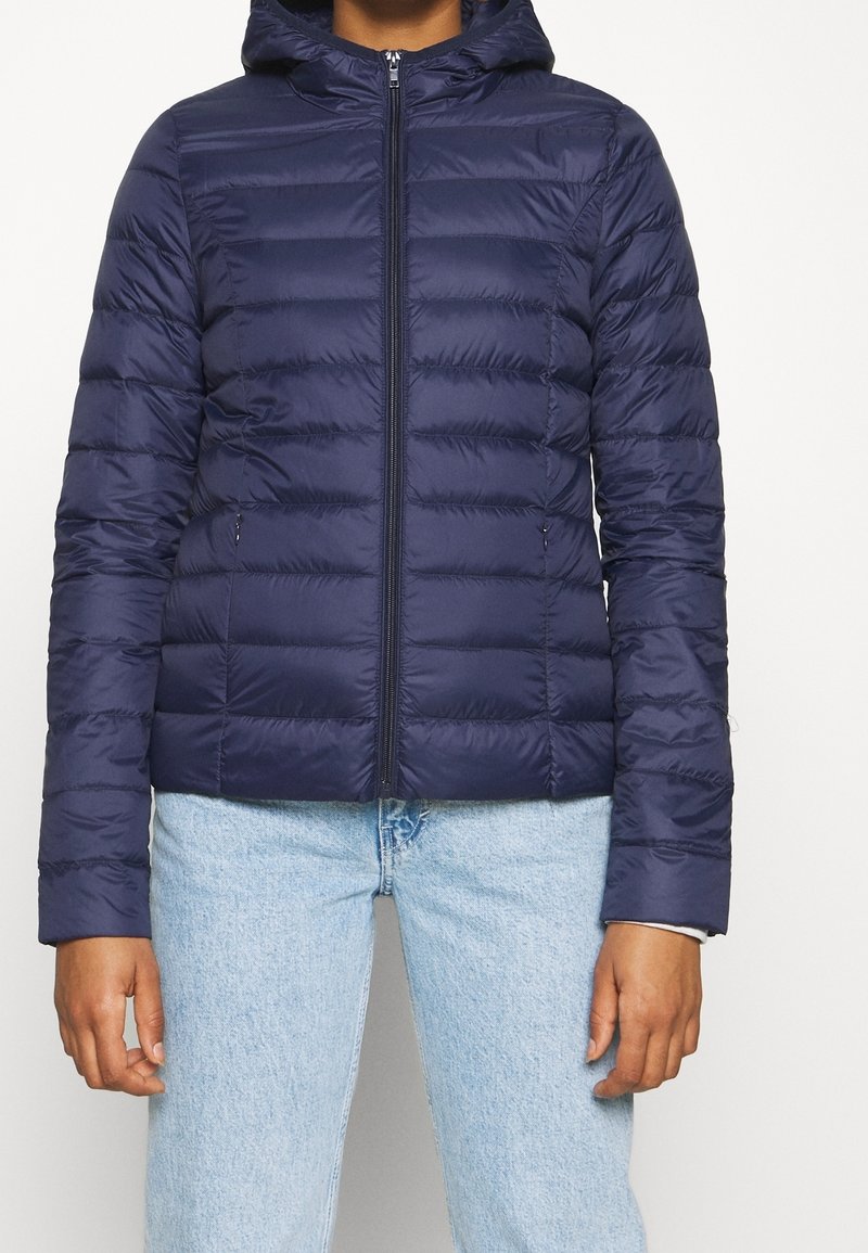 Chaqueta de plumas de color navy con capucha, que presenta un diseño de acolchado horizontal, cierre de cremallera y dos bolsillos laterales. Material suave y ligero.