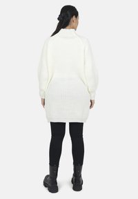 Hvid strikket sweater med høj krave, oversized pasform og ribbet tekstur, parret med sorte leggings og ankelstøvler.
