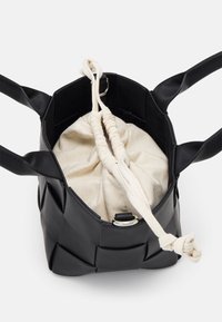 Svart vävd handväska som har en mjuk inre dragsko-påse med ett beige tygfoder. Inkluderar två svarta handtag för enkel bärning.