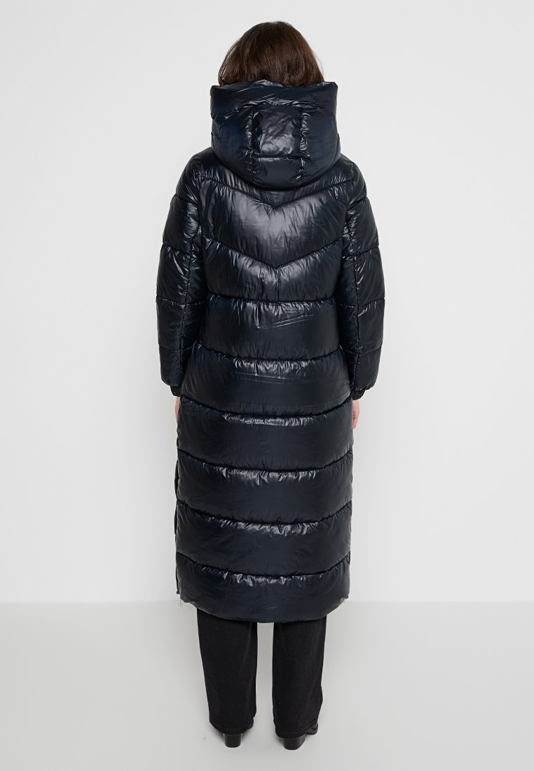 Manteau long et bouffant en matériau brillant navy, avec une capuche, un motif de couture en chevron et une coupe jusqu'aux genoux. Texture lisse.
