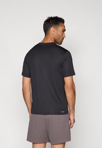 Svart atletisk t-skjorte med korte ermer og glatt tekstur, med rund hals, kombinert med grå mesh-shorts, sett bakfra.