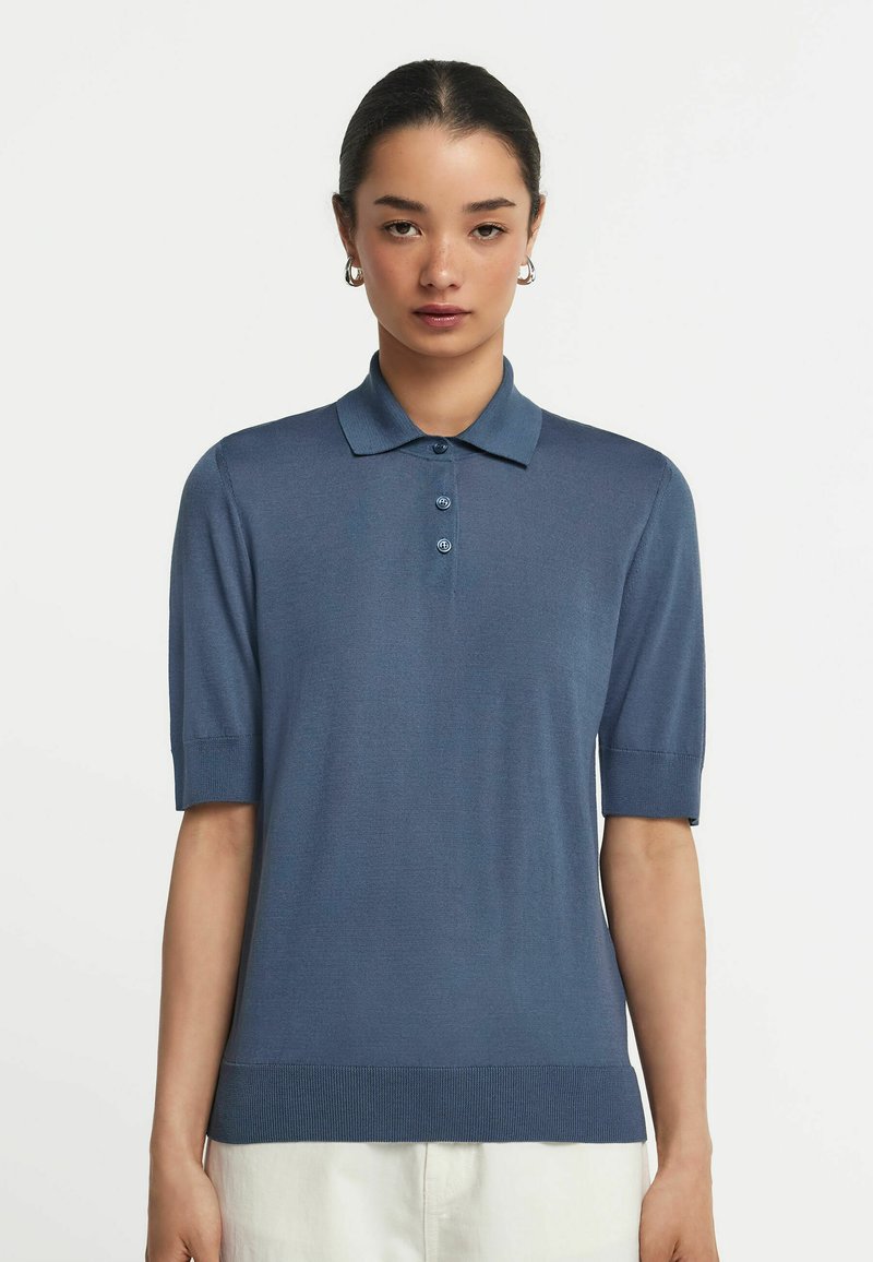 Blå stickad polo skjorta med korta ärmar, en klassisk krage och ribbad nederkant. Knapparna fram ger detaljer till den minimalistiska designen.