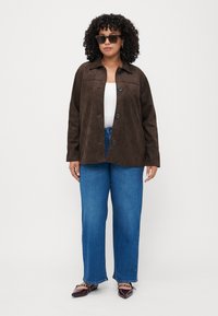 Brahms zamaka pogumēts jaka ar apkakles kaklu, apvienota ar zilām platas kājas biksēm un tumšām norādēm. Tekstūrēta auduma ar redzamām šuvēm.