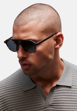 Gafas de sol con un elegante marco negro, lentes oscuros y un ligero degradado. Camiseta de polo gris texturizada con un cuello bajo y un patrón acanalado.