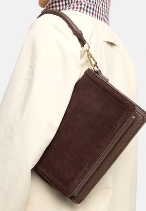 Osoba w kremowych spodniach i koszuli w kratę, niosąca na ramieniu ciemnobrązową zamszowo-skórzaną torebkę z złotym zapięciem.