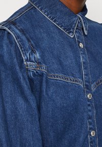 Jeansskjorta med en blå tvätt, med klassisk krage, framknappar och subtila veck vid axlarna för extra textur.