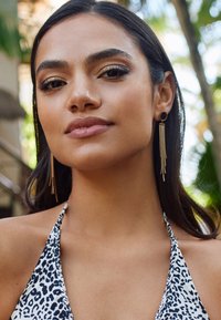 Gold tassel earrings with circular studs, worn with a halter neck top featuring a black and white leopard print pattern.