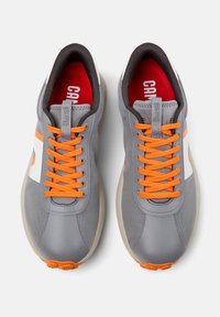 Sneakers grigi con lacci arancioni, logo bianco, tessuto testurizzato, colletto imbottito e suola in gomma con dettagli di trazione. Soletta rossa visibile.