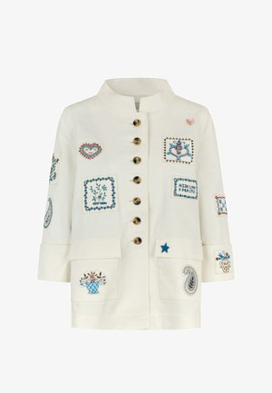 Witte jas met een hoge kraag, voorzien van diverse kleurrijke geborduurde badges, gouden knopen en twee grote voorzakken.