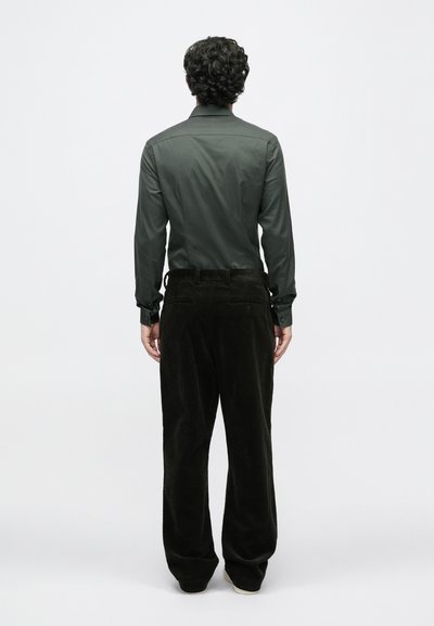 Sötétzöld gombos ing sima textúrával, széles lábú kordbársony nadrággal párosítva sötét árnyalatban, hátizsebekkel és övhurkokkal.