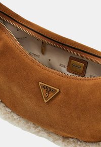 Borsa a mano in suede beige con fodera testurizzata crema, hardware dorato e logo triangolare. Presenta una chiusura a zip con un comodo pull tab.