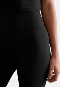 Schwarze, hochtaillierte Leggings aus glattem, elastischem Stoff. Verfügt über ein dezentes Logo und eine enge Passform für Komfort bei Aktivitäten.