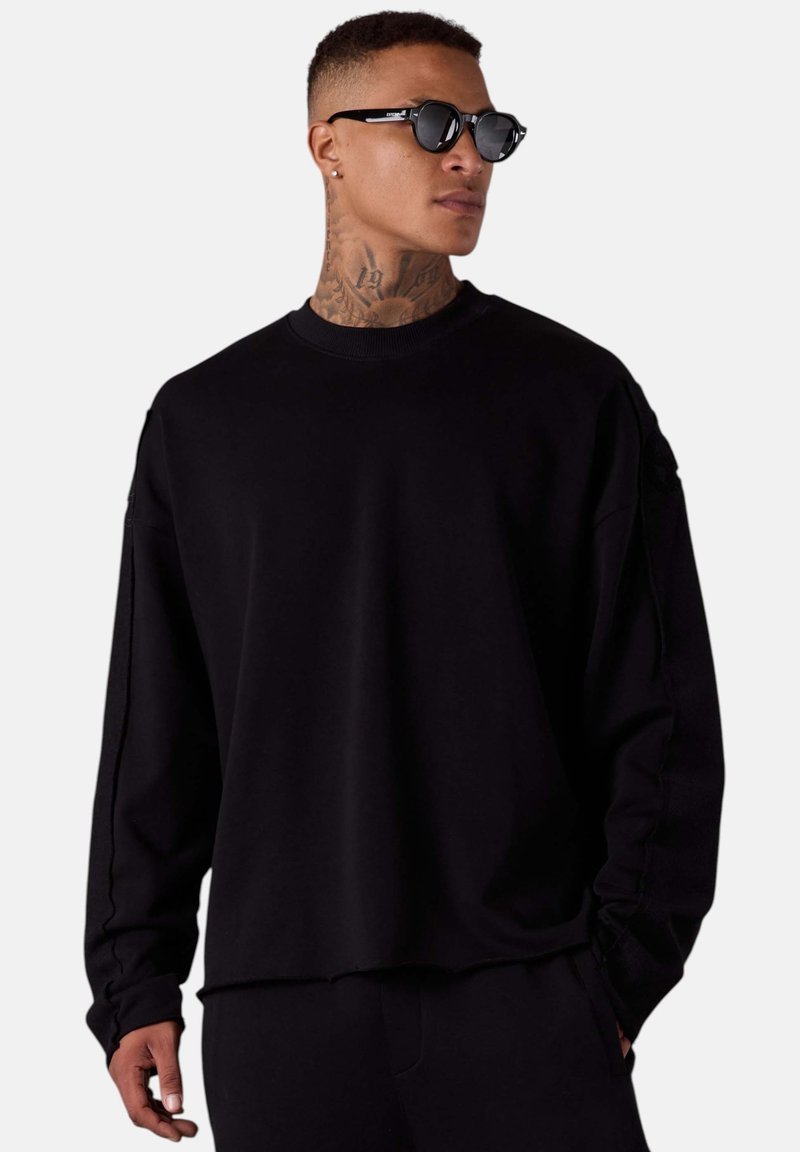 Sweatshirt noir surdimensionné avec des manches longues, un col rond côtelé et des détails de couture subtils. Il présente une coupe décontractée et une texture douce.