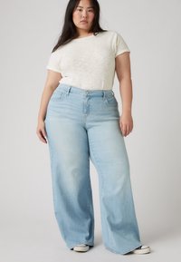 Light blue wide-leg jeans with a high waist and front pockets, paired with a short-sleeve off-white textured t-shirt.