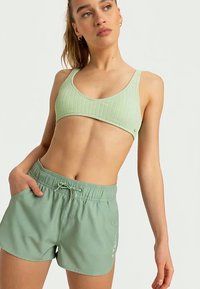Soutien-gorge de sport côtelé vert clair associé à un short ample assorti. Le short présente une taille élastique et un cordon de serrage décoratif.