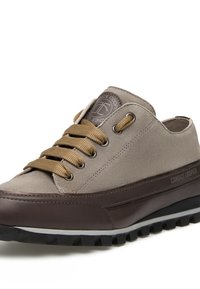 Sneaker grigia in suede con dettagli in pelle marrone, punta rotonda, lacci beige e patch del logo sulla linguetta; suola in gomma testurizzata con scanalature.