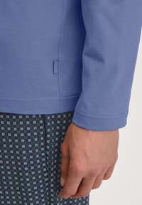 Lange mouwen, lichtblauwe blouse gemaakt van zachte stof, met een zijlabel en aansluitende manchetten, gecombineerd met een donkere, gebloemde broek.