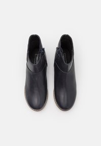 Tmavě modré kožené kotníkové boty s kulatou špičkou, bočními zipy a béžovým prošíváním podešve. Hladký povrch, minimalistický design bez viditelných ozdob.