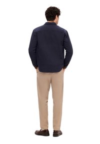 Camisa azul marino abotonada con cuello, mangas largas y corte cuadrado, combinada con pantalones color caqui y zapatos marrones. Textura suave, diseño sencillo.